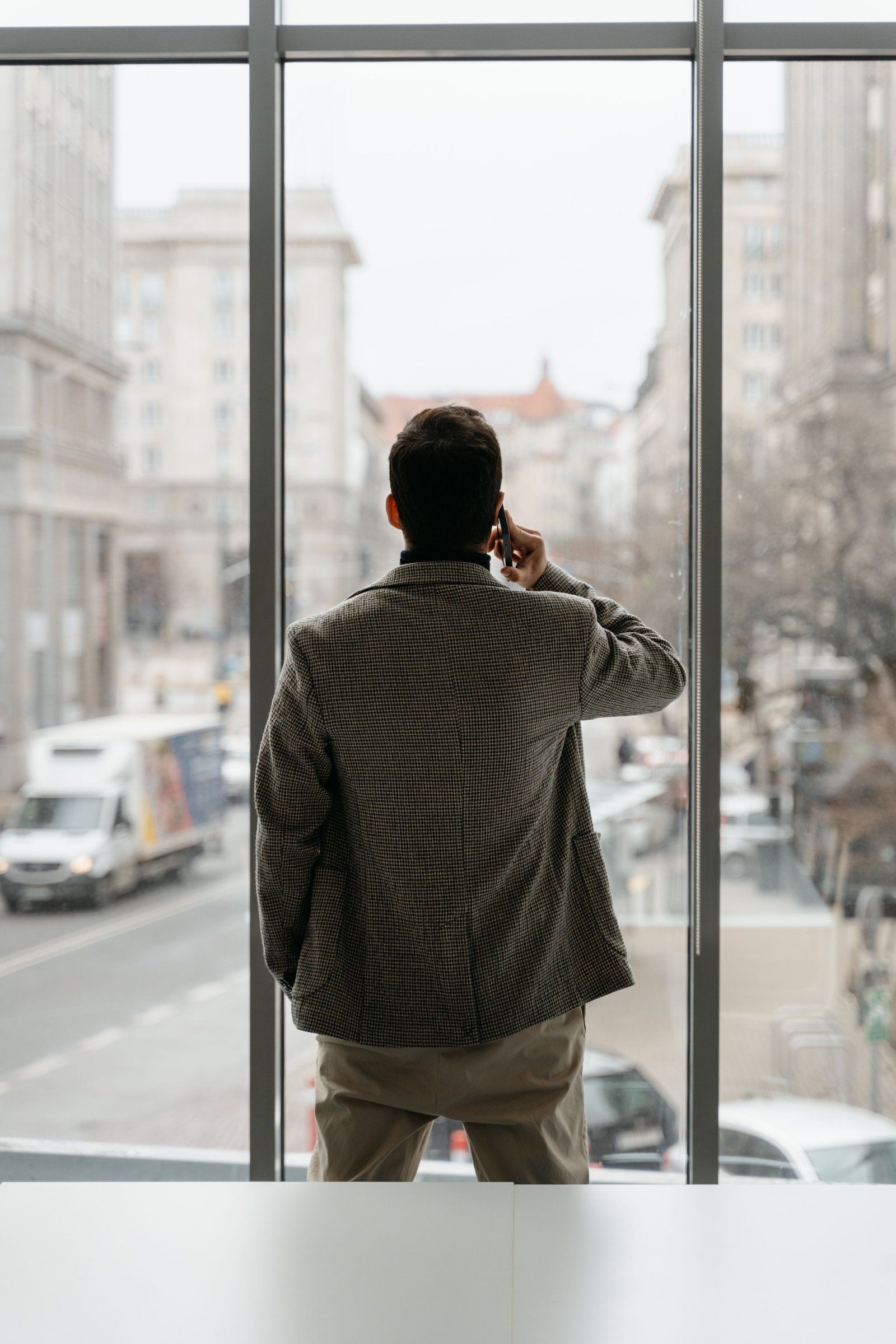A person seen from behind making a phone call at an office window above a city street
