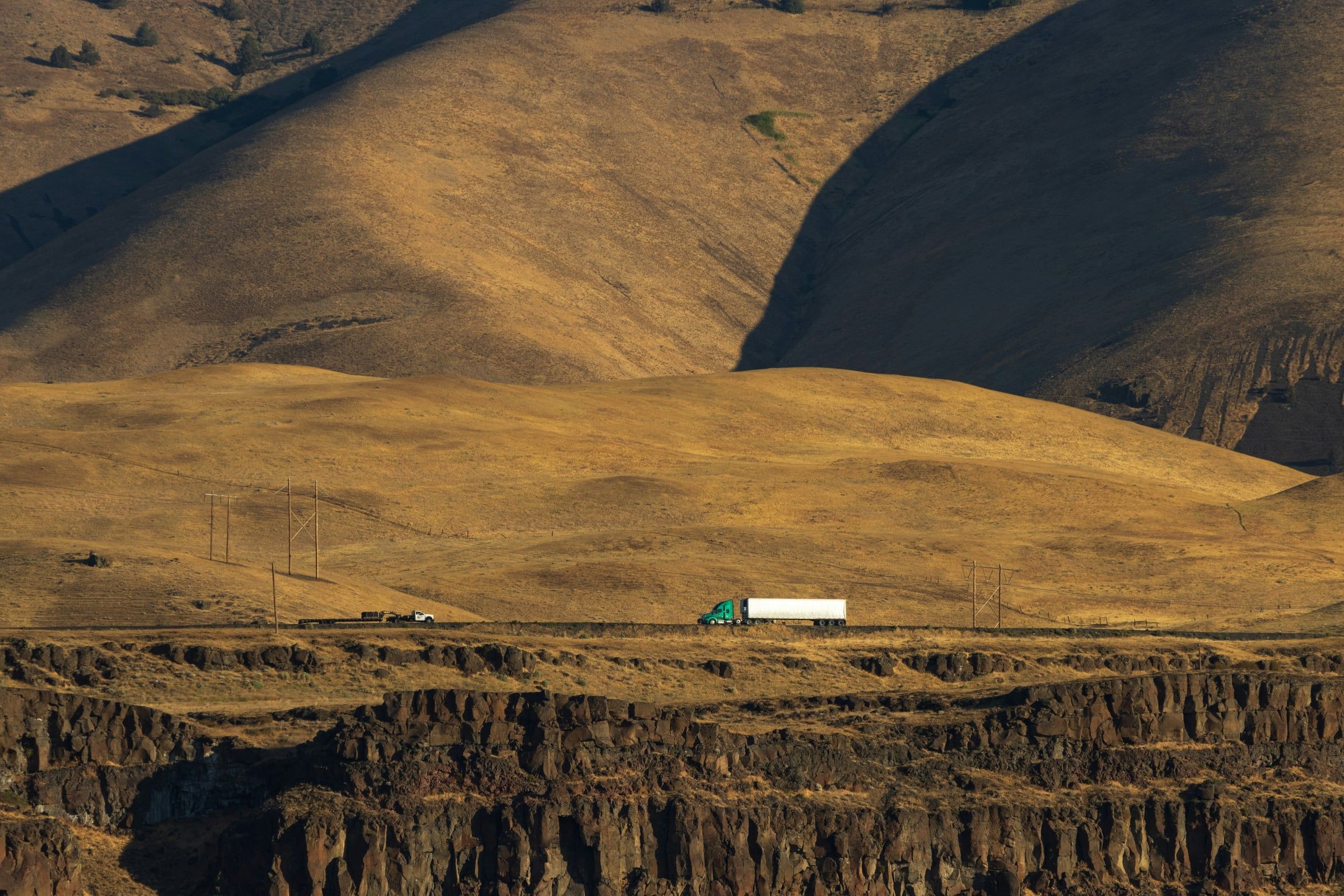 A tractor-trailer on a highway through golden desert hills
