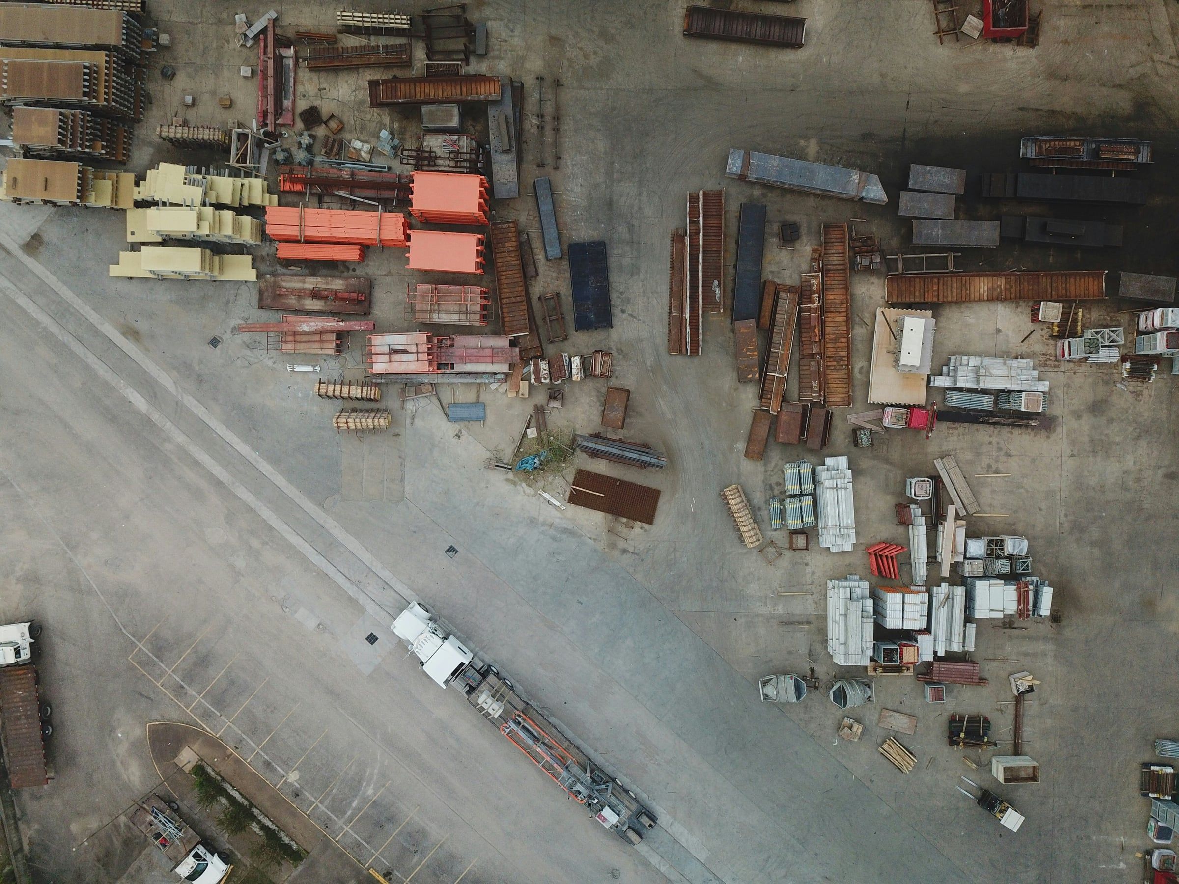 Aerial view of a materials yard with a loaded flatbed trailer leaving